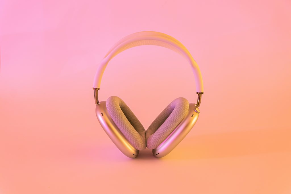 Rose gold over-ear wireless headphones on a pink to orange gradient background.